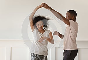Happy young african couple holding hands dancing laughing at home