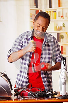 Happy Young African Ecuadorian male Technician fixing a red sander with his screwdriver on office background