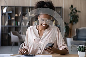 Happy young african ethnic woman paying bills in mobile app.