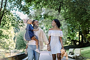 Happy young african family spending time outdoor in park on a summer day. Joyful smiling couple holding hands and