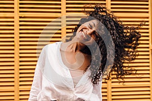 Happy young african girl looking at camera smiling with teeth waving her hair on yellow background.