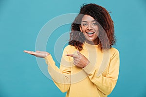 Happy young african lady dressed in warm sweater pointing.