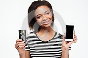 Happy young african lady using phone and holding debit card.