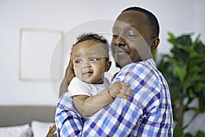 happy young African man playing with his little baby while lying in bed