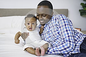 happy young African man playing with his little baby while lying in bed