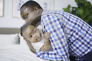 happy young African man playing with his little baby while lying in bed