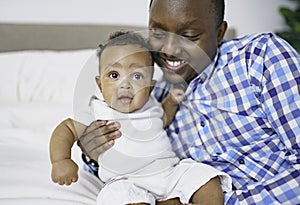 happy young African man playing with his little baby while lying in bed