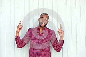 Happy young african man pointing upwards by wall