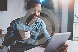 Happy young African man reading world news by digital tablet while sitting at the table on a sunny morning.Concept of