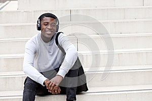 Happy young african man sitting on steps and listening to music with headphones