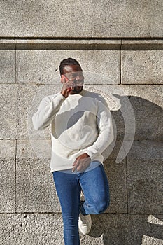 Happy young African man using cell phone and smiling leaning against a wall. Latino talking on the phone.