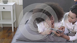 Happy young African mother using tablet computer with daughter for education and learning on bed.