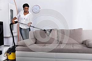 African Woman Cleaning Sofa With Vacuum Cleaner photo