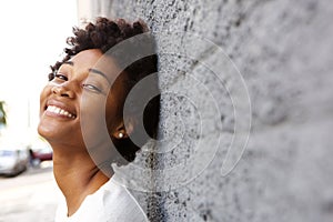 Happy young african woman leaning to a wall