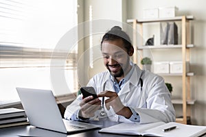 Happy young Afro American doctor chatting online on mobile phone