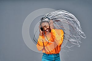 Happy young Afro American lady relaxed with great song, has broad smile, touches headphones, listens music, dressed in yellow