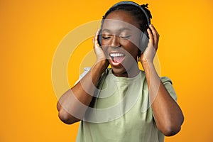 Happy young Afro American woman listening to music in headphones against yellow background