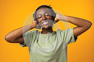 Happy young Afro American woman listening to music in headphones against yellow background