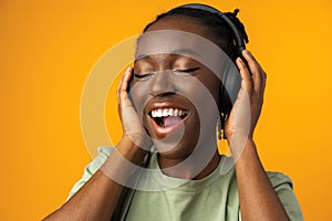 Happy young Afro American woman listening to music in headphones against yellow background