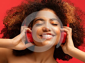 Happy young Afro American woman relaxed with great song, has broad smile, touches headphones, listens music