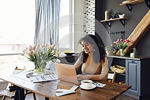 Happy young afro american woman sitting at home using laptop and typing on keyboard. Smiling female student or freelancer looking