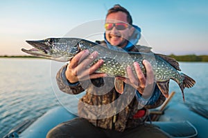 Happy young angler holds the pike fish