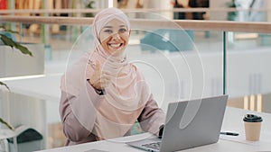 Happy young arab businesswoman sitting at office desk typing on laptop working on internet checking new app smiling