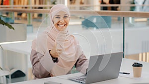 Happy young arab businesswoman sitting at office desk typing on laptop working on internet checking new app smiling