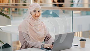 Happy young arab businesswoman sitting at office desk typing on laptop working on internet checking new app smiling