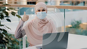 Happy young arab businesswoman sitting at office desk typing on laptop working on internet checking new app smiling