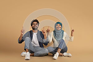 Happy Young Arab Couple Pointing Up At Copy Space Above Their Heads