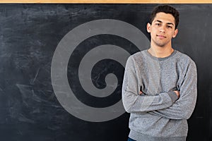 Happy young arab man standing with crossed arms on blackboard background, education concept, serious male teacher or