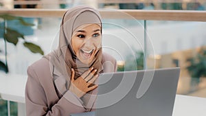Happy young arab woman sitting at desk receiving email on laptop with good news shocked excited girl rejoices in victory