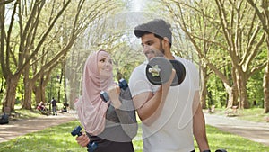 Happy young arabian couple in sport clothes having morning workout at summer park with dumbbells. Active man and woman
