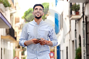 Happy young arabic man laughing with mobile phone and earphones in the city