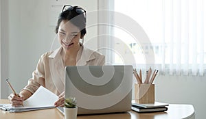 Happy young asia business woman entrepreneur using computer looking at screen working in internet sit at office desk, smiling