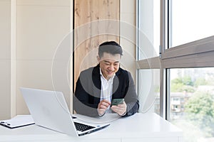 Happy young Asian business man in office looking at mobile phone, with emotion winner or win, financial stock sports betting.