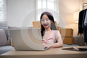 Happy young asian business owner woman prepare parcel box and check online order of product for deliver to customer on