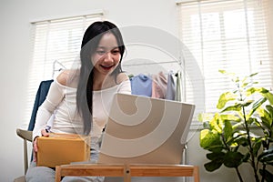 Happy young asian business owner woman prepare parcel box and check online order of product for deliver to customer on