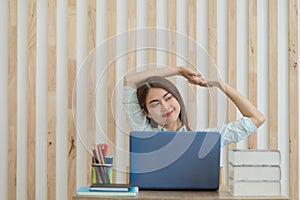 Happy young Asian business woman relaxing with hands behind her head while working in office