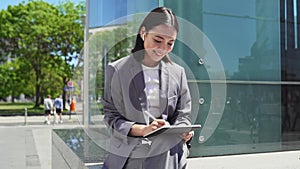 Happy young Asian business woman using digital tablet working outdoors.