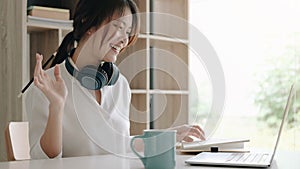 Happy young asian business woman waving hands to greeting partner during making video conference with her team