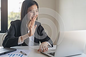 Young asian business woman waving hands to greeting partner during making video conference with her team