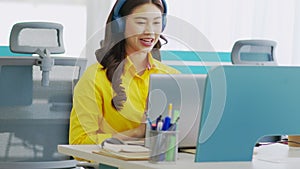 Happy young asian business woman wears headset talk to online video conference call with her business team at modern office or Co-