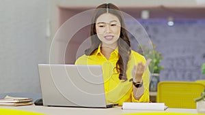 Happy young asian business woman wears yellow shirt meeting online video conference call with her business team at modern office