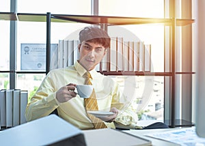 Happy young asian businessman in formal drink coffee sitting in modern workplace in break time