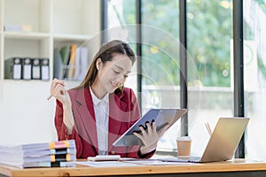 Happy young asian businesswoman celebrating success with arms raised in front of laptop with excitement at office