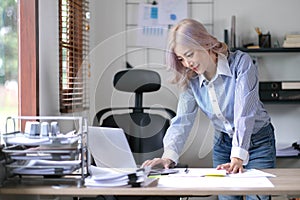 Happy young Asian businesswoman standing using calculator and laptop computer at office.