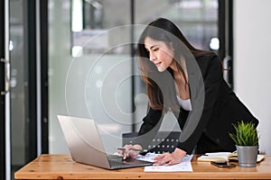 Happy young Asian businesswoman standing using laptop computer at office.