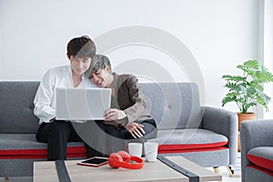 Happy young Asian couple gay lovers sitting snuggle and using laptop computer together on sofa at living room